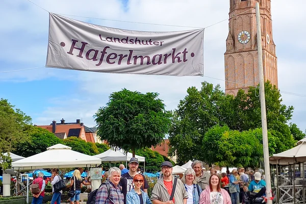 Menschengruppe am Haferlmarkt mit großem Transparent der Veranstaltung und Kirche im Hindergrund