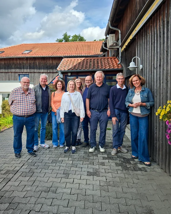 Gruppe von Menschen draussen an einer Holzwand eines Hauses