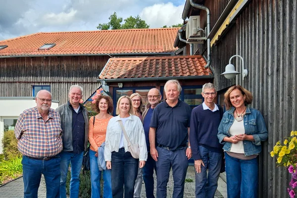Gruppe von Menschen draussen an einer Holzwand eines Hauses