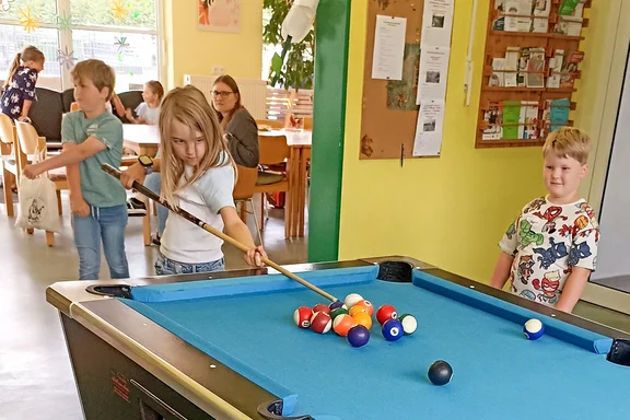 Kleines Mädchen beim Billard spielen an einem großen Pooltisch