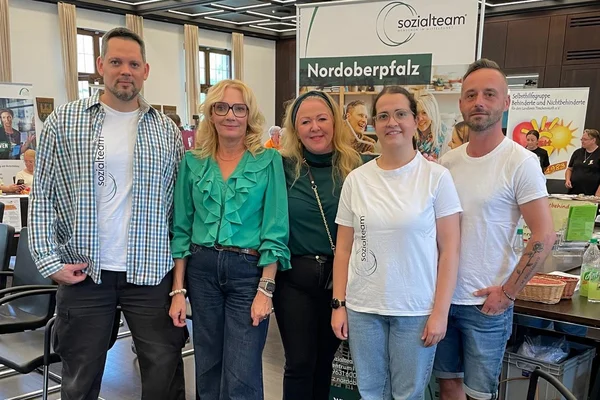 Gruppe von 5 Mitarbeitern des Sozialteams vor einem Werbedisplay 
